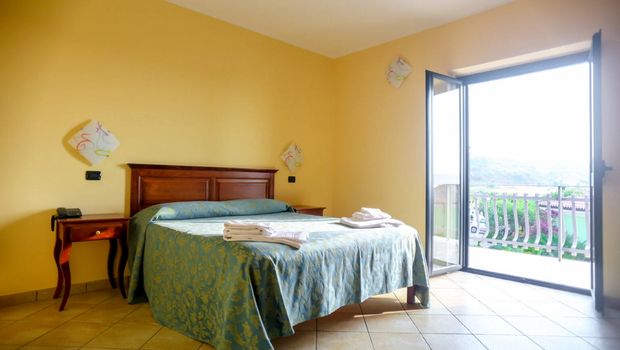 Helles Zimmer mit mediterranem Flair, gemütlichem Doppelbett und direktem Zugang zum Balkon mit Ausblick ins Grüne.