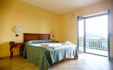 Helles Zimmer mit mediterranem Flair, gemütlichem Doppelbett und direktem Zugang zum Balkon mit Ausblick ins Grüne.