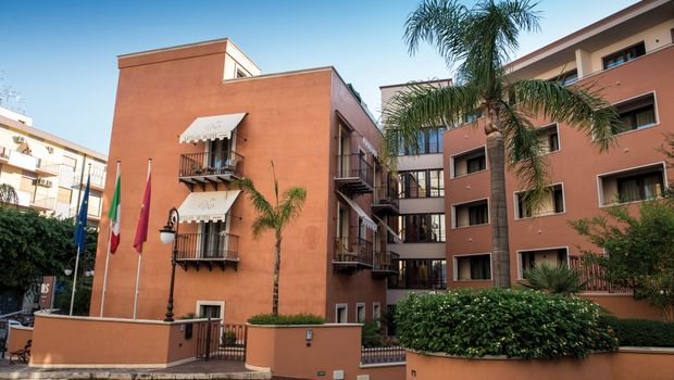 Einladende Außenansicht des Artemis Hotels mit mediterranem Flair, Palmen und kleinen Balkonen – zentral gelegen für einen entspannten Urlaub in Italien.