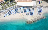 **Alt-Text:** Luftaufnahme eines Strandes mit türkisblauem Wasser und vielen blauen Sonnenschirmen.