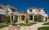Charmante Hotelanlage im mediterranen Stil mit liebevoll gepflegtem Garten, hellen Fassaden und einem dekorativen Rundbogen aus Naturstein.