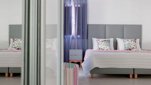 Modern eingerichtetes Doppelzimmer mit grauem Bettkopfteil, floral gemusterten Kissen, sanften Pastelltönen und lichtdurchflutetem Ambiente – ideal für entspannte Urlaubstage.