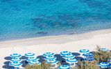 Reihe von blau-weißen Sonnenschirmen an einem feinsandigen Strand mit kristallklarem Wasser in verschiedenen Türkistönen.