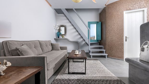 Modern eingerichtetes Maisonette-Zimmer mit grauem Sofa, Holztisch, dekorativer Wendeltreppe und stilvollen Akzenten – helle Farben und mediterrane Details schaffen eine elegante Wohlfühlatmosphäre.