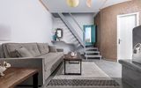 Modern eingerichtetes Maisonette-Zimmer mit grauem Sofa, Holztisch, dekorativer Wendeltreppe und stilvollen Akzenten – helle Farben und mediterrane Details schaffen eine elegante Wohlfühlatmosphäre.