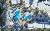 Luftaufnahme einer weitläufigen Hotelanlage mit mehreren Pools, Palmen, Liegeflächen und hellen Gebäuden im kykladischen Stil – harmonisch eingebettet in eine mediterrane Landschaft.