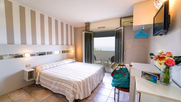 Modern eingerichtetes Zimmer mit gemütlichem Doppelbett, dezenten Farbakzenten und direktem Zugang zum Balkon mit Meerblick – ideal für entspannte Urlaubsmomente.