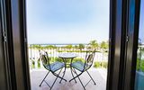 Balkon mit zwei Eisenstühlen und Tisch, Blick auf Poolanlage und das Meer in der Ferne.