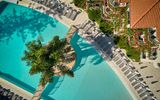 Draufsicht auf einen eleganten Pool mit Palmeninsel und umliegenden Liegestühlen – eine stilvolle Urlaubsoase direkt am Hotel.