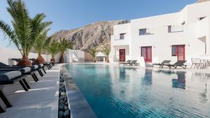 Moderner Poolbereich mit stilvollen Liegen und Palmen, umgeben von weißer Architektur und beeindruckender Bergkulisse – ideal zum Entspannen unter der griechischen Sonne.