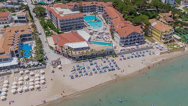 Luftaufnahme eines belebten Strandhotels mit großem Poolbereich, Sonnenschirmen am Strand und direkter Lage am klaren Meer.