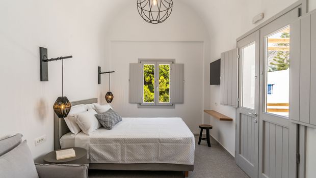 Helles und modern eingerichtetes Doppelzimmer mit schlichter Eleganz, gemütlichem Bett, stylischen Lampen und Blick auf grüne Pinien durch das Fenster.