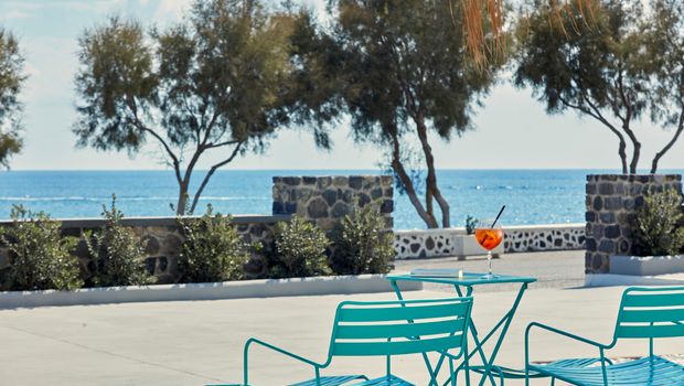 Zwei türkisfarbene Loungestühle und ein Tisch mit Aperol Spritz vor traumhafter Meereskulisse – entspannte Urlaubsatmosphäre direkt am Wasser.