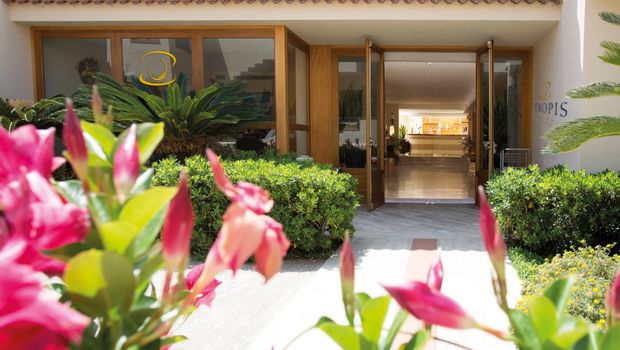 Einladender Hoteleingang mit gepflegter Gartenanlage, blühenden Blumen und offen gestalteter Lobby.
