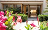 Einladender Hoteleingang mit gepflegter Gartenanlage, blühenden Blumen und offen gestalteter Lobby.
