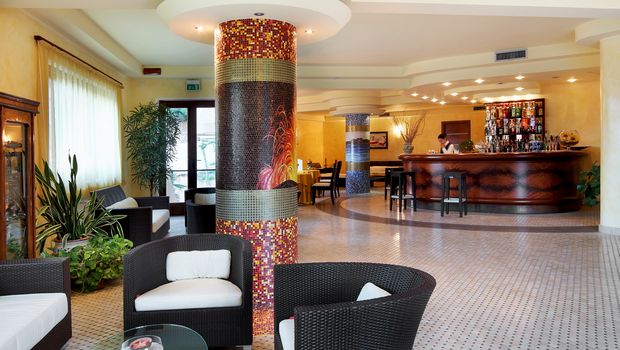 Heller Hotel-Loungebereich mit gemütlichen Sitzgruppen, stilvoller Mosaiksäule und eleganter Bar mit großer Getränkeauswahl – freundliches Ambiente mit modernen und klassischen Elementen.
