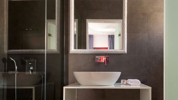 Modernes Badezimmer mit edlen dunklen Fliesen, stilvollem weißen Waschbecken auf einem minimalistischen Waschtisch und beleuchtetem Spiegel – ein eleganter Ort zum Frischmachen.