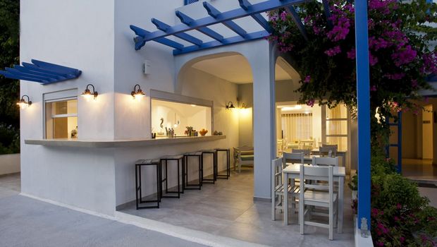 Gemütliche Außenterrasse mit Bar und Sitzgelegenheiten unter einem blauen Holzpergola, geschmückt mit blühender Bougainvillea – ideal für entspannte Abende in mediterranem Ambiente.