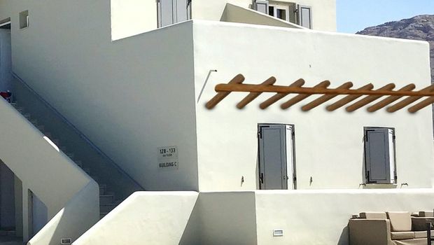 Traditionell weißes Gebäude mit typischer kykladischer Architektur und gemütlichem Sitzbereich am glitzernden Pool – perfekter Ort zum Entspannen unter der Sonne Santorins.