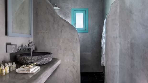 Modernes Badezimmer mit glatten Betonwänden, offenem Duschbereich und stilvollem Naturstein-Waschbecken – minimalistische Gestaltung mit hochwertigen Materialien.