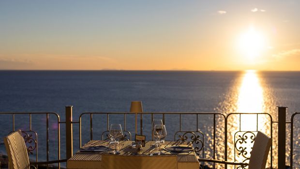 Romantisch gedeckter Tisch für zwei mit Meerblick bei Sonnenuntergang – Weingläser, Besteck und warme Lichtstimmung.