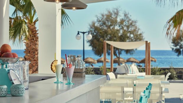 Stilvolle Outdoor-Bar mit erfrischenden Cocktails, weißen Sitzmöbeln und direktem Blick aufs Meer – perfekt für einen entspannten Nachmittag unter Palmen.